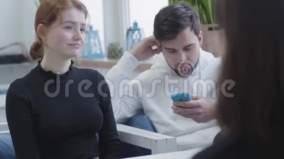 三个朋友坐在一家咖啡馆或一个中心在休息时聊天和微笑而男人在打短信等待视频的预览图