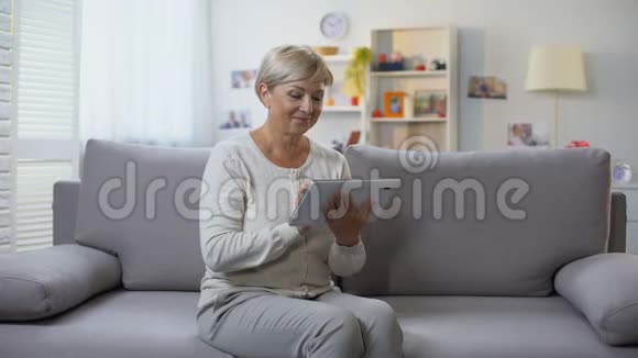 退休女性滚动平板电脑应用程序在家放松网上购物视频的预览图