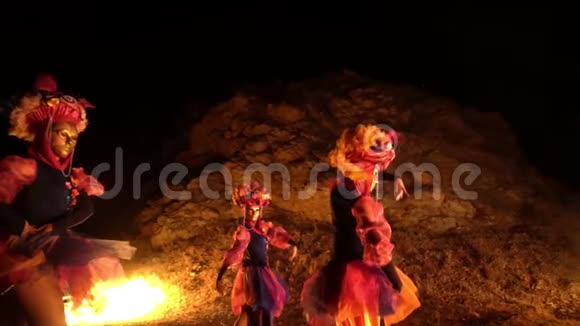 三个穿着五颜六色民族服装的女孩在山坡的背景下在明亮的炉火旁跳舞视频的预览图