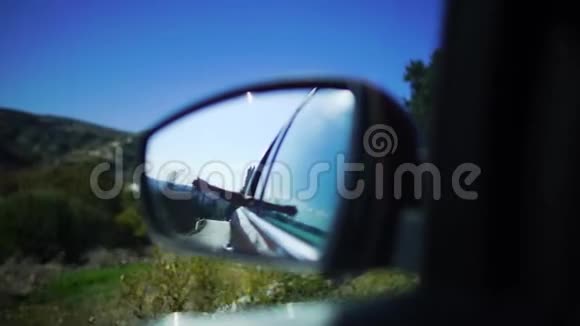 阳光大道行驶中手不认乘客在汽车侧后视镜中的反射视频的预览图