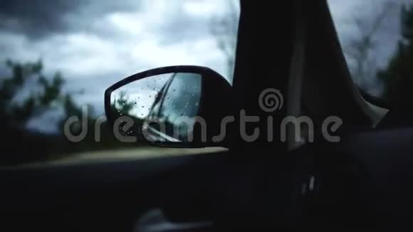 在秋天美丽的道路上一辆移动的汽车在行驶中的侧镜中反映了雨天的黄昏街道视频的预览图