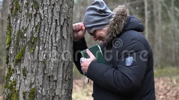 悲伤的人带着圣经和念珠在树旁哭泣视频的预览图