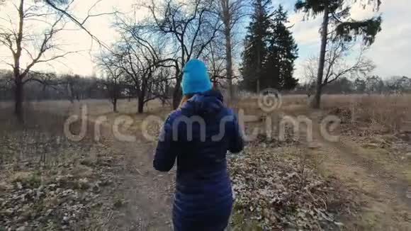 穿着蓝色外套的年轻女子在春天公园散步视频的预览图