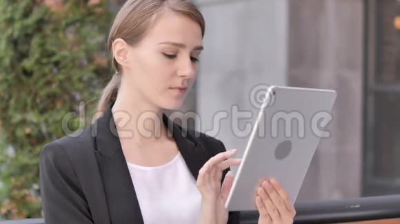 坐在户外为平板电脑的成功欢呼的年轻女商人视频的预览图