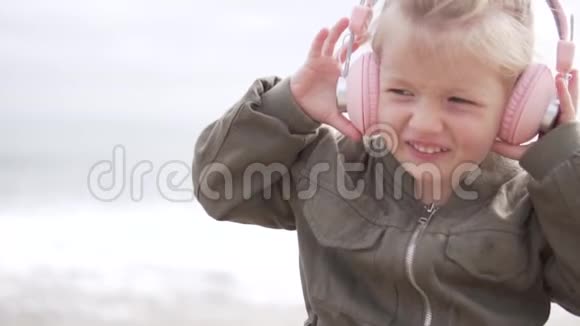 可爱的小女孩在海边用耳机听音乐视频的预览图