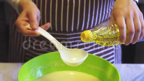 在家庭厨房的绿色碗里女性手的特写慢动作将葵花籽油添加到面糊中烹饪煎饼视频的预览图