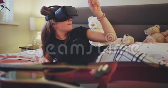 在一个现代的青少年房间里漂亮的女士在玩虚拟现实眼镜探索她躺在上面的虚拟世界视频的预览图