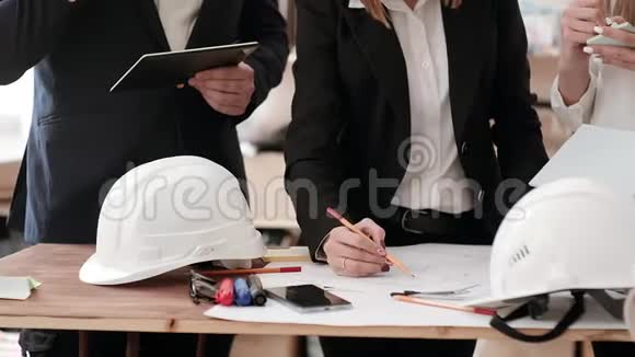 穿着商务服的工程师站在一张桌子旁桌子上放着蓝图头盔铅笔记号笔他们视频的预览图