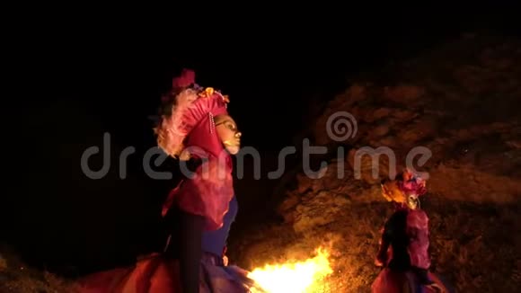 一个夜晚在燃烧的火焰附近三个穿着五颜六色服装的女孩和金色的舞蹈视频的预览图