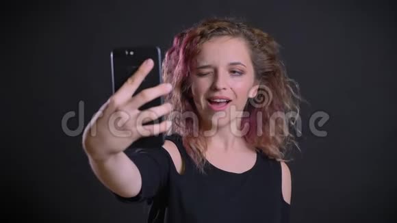快乐的年轻白种人女孩的肖像粉红色的头发制作自拍照片使用智能手机在黑色背景视频的预览图