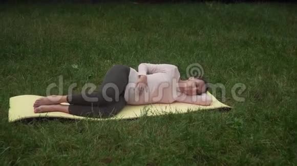 一位孕妇在公园里做瑜伽躺在左边的一个姿势阿萨娜沙瓦萨纳一个死男人的姿势视频的预览图