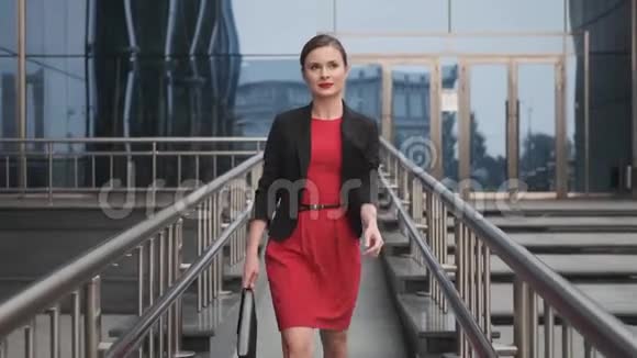 自信的商务女性穿着红色连衣裙走在商务中心旁边穿着红色裙子的年轻女子视频的预览图