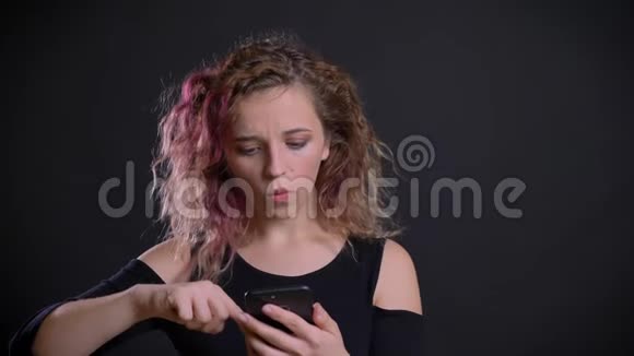 年轻的白种人女孩的画像她的粉红色头发看着她的智能手机对黑色感到惊讶和不安视频的预览图