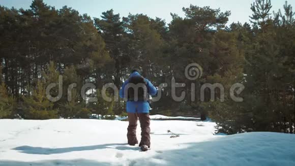 冒险男子徒步旅行者穿着温暖的衣服和背包走在雪覆盖的道路上松林一个人走过视频的预览图