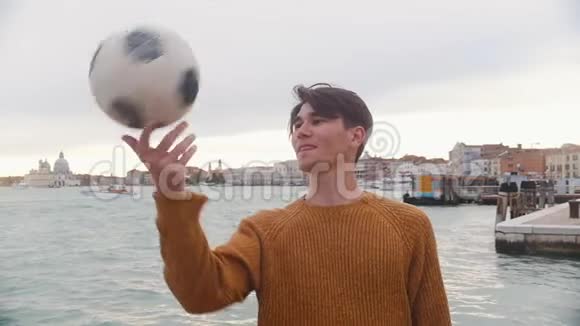 一个年轻人在海边的看台上玩足球把球旋在他的手指上视频的预览图