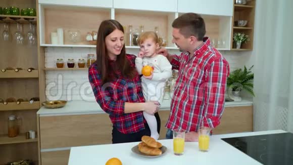 幸福的家庭和蹒跚学步的女孩在厨房喝橙汁视频的预览图