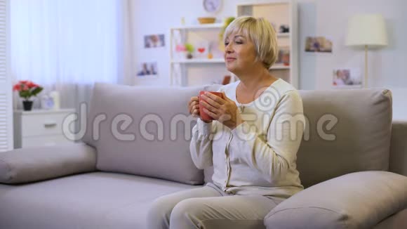 漂亮的老太太坐在家里的沙发上喝茶享受周末视频的预览图