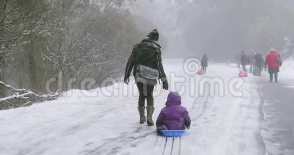 妈妈拖着一个小男孩走在雪地上的路上视频的预览图