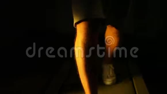 在黑暗中走在跑步机上的人腿的特写视频的预览图