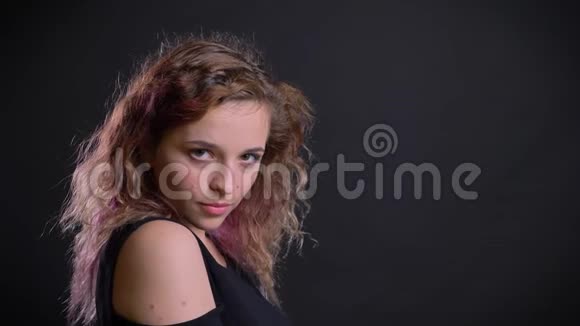 年轻的白种人粉红色的女孩在黑色背景下调情摆姿势把头发摇成相机的肖像视频的预览图