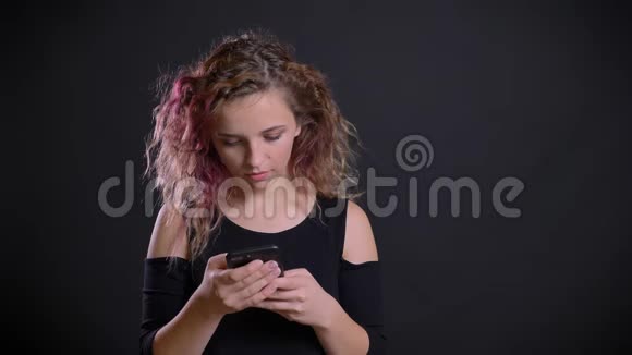 年轻的白种人女孩的肖像粉红色的头发专注地看着她的智能手机在黑色的背景视频的预览图