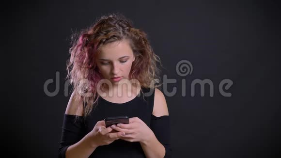在黑色背景下年轻的白种人女孩带着粉红色的头发看着她的智能手机这幅严重的乐趣视频的预览图