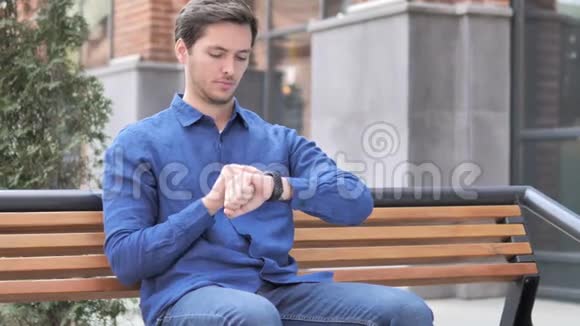 年轻人使用智能手表户外坐凳视频的预览图