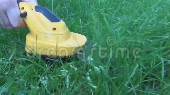 女性的手在空地上剪一块绿色的草坪上面有一个带有黄色身体的电动修剪器和一个带有牙齿的短喷嘴视频的预览图
