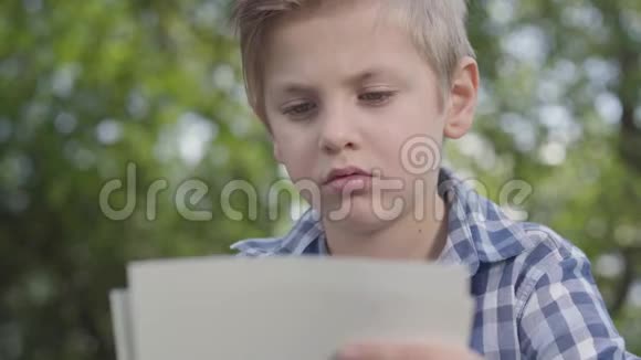一幅可爱的英俊男孩穿着格子衬衫看公园里的纸的画像户外夏日休闲视频的预览图