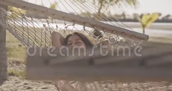 在棕榈树下的热带海滩吊床上的女人异国情调放松生活方式广告商业理念视频的预览图