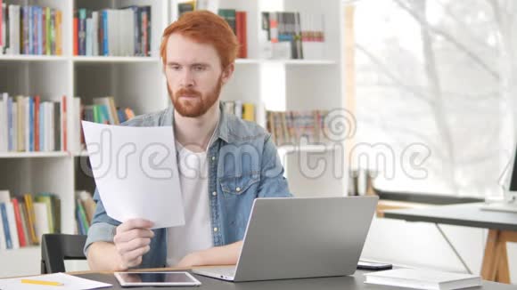 临时红发男子在工作中阅读合同视频的预览图