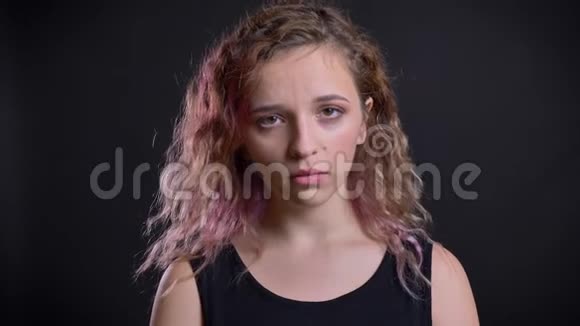 一幅年轻的白种人女孩带着粉红色的头发看着镜头在黑色的背景下绝望地悲伤视频的预览图