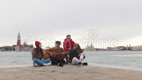 一群年轻的朋友坐在码头的边缘唱歌一个弹吉他的男人视频的预览图