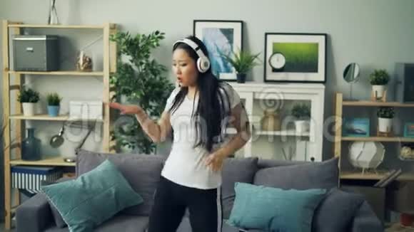 美丽的年轻女士在家跳舞戴着耳机唱歌独自在客厅听音乐视频的预览图