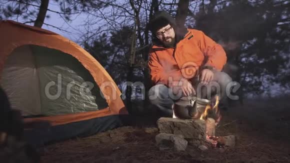 一个人坐在火旁有一个水壶里面有水沸腾视频的预览图