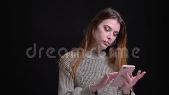 年轻漂亮的白种人女性在手机上上网然后看着相机微笑着的特写照片视频的预览图