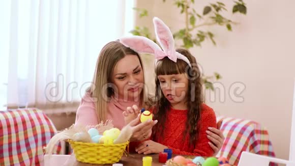 小心的妈妈拿着复活节彩蛋她的女儿用手指蘸着颜料在你脸上微笑视频的预览图
