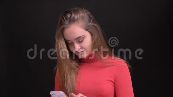 年轻美丽的黑发女性在手机上浏览然后看着相机开心地笑着的特写照片视频的预览图