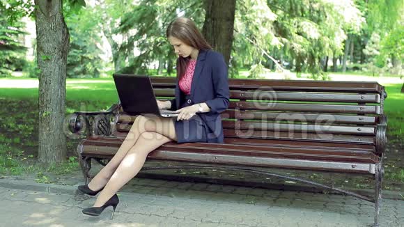 年轻商务女性手提电脑工作在公园长椅上视频的预览图