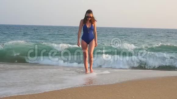 年轻女子从海洋走到海滩背景是波浪穿着泳装的漂亮女孩踏上大海视频的预览图