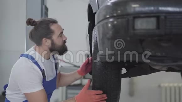 在维修服务站检查举升汽车车轮上的悬挂或刹车的长胡子技工视频的预览图