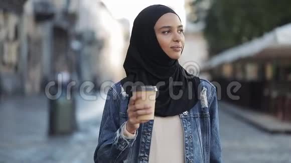 美丽的年轻穆斯林妇女一个迷人的外表喝咖啡走在城市的街道上视频的预览图