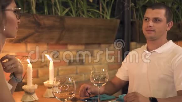 一对年轻夫妇坐在桌上拿着蜡烛在餐厅里吃着浪漫的晚餐晚上喝酒的男女视频的预览图