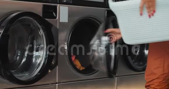 年轻的非洲裔美国妇女坐在洗衣机前拿走洗衣服自助服务公众视频的预览图
