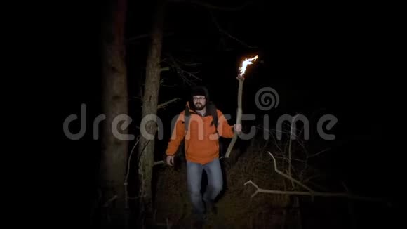 一位游客在树林里迷路了一个穿着明亮夹克手里拿着燃烧的火炬的人在夜晚穿过一个视频的预览图