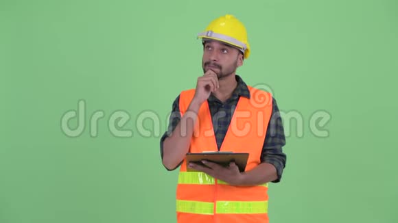快乐的年轻胡子波斯建筑工人一边拿着剪贴板一边思考视频的预览图