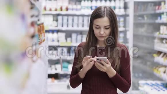 年轻女性在超市购物使用智能手机查看购物清单视频的预览图
