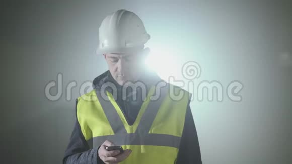 穿着建筑制服和头盔的人在黑色背景前用手机说话的肖像视频的预览图
