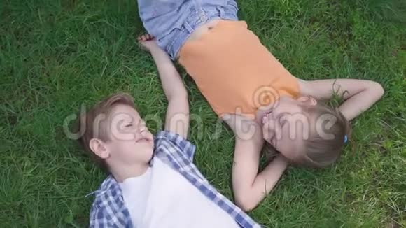 两个有趣的孩子躺在公园的草地上互相微笑抓住男孩的女孩一对快乐视频的预览图