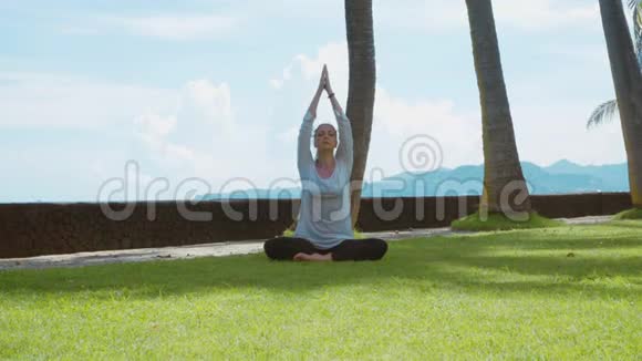 年轻女子做瑜伽练习在巴厘岛的海洋海滩上放松莲花姿势美丽的背景和自然的声音视频的预览图